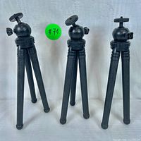 Front view of three black mini tripods with adjustable legs and ball heads, displayed upright on a white surface.