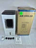 Air Cooler with remote, box, manual and four black accessories laid out on white surface.