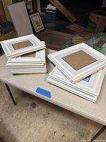Stack of white picture frames on table, showing two sizes.