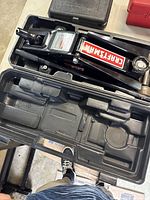 View of Craftsman trolley jack in black molded carrying case on gray table. Shows lifting arm and handle.