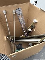 Curtain rods of various sizes with ornate finials in a large cardboard box, including packaged mounting hardware.