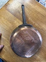 View of pan bottom showing hammered copper with patina and wear marks on wooden surface.