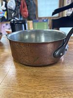 Side view of a small copper saucepan showing hammered copper body and long metal handle with slight patina