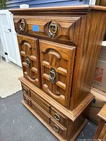 Front and side angled view of the tallboy dresser showing drawer and cabinet door details and metal ring handles