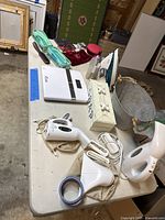 Wide view of the household items on a table including steamers, iron, scale, pail, and soapbox.
