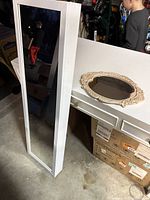White wall-mounted jewelry armoire with front glass mirror leaning against a white cabinet, boy reflected in mirror