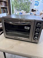 Front view of KitchenAid toaster oven showing stainless steel body, glass door with handle, and manufacturer label below door.