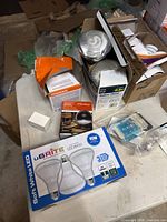 Photo showing a table with mostly full open boxes of various light bulbs including uBRITE LED bulbs, CFL spiral bulbs, and Sylvania ECO LED bulbs.