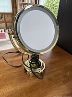 Front view of the gold-tone lighted magnifying mirror on stand with power cord.