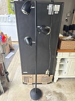 Full view of the black metal floor lamp showing three directional light heads and round base, approximately 60 inches tall.