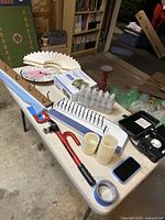 Long white ceiling medallion, small plastic bottles, an outdoor timer, two pillar candles, tape, and miscellaneous household items on a table.