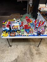 Full view of all Paw Patrol vehicles and figures arranged on a table including trucks, planes, helicopters, and small character figures in front.
