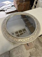 Front view of the round mirror showing the detailed ornamental silver frame and reflective surface.