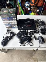Overall view of Sega Genesis console, controllers, power adapter, and game cases stacked vertically.