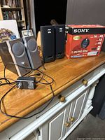 Photo showing both sets of computer speakers and the Sony DVD-RAM drive box on a wooden table.
