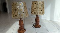 Two wood and capiz shell table lamps with geometric shades standing on tiled floor.