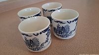 Four white ceramic tea cups with blue traditional design placed on a beige surface to show overall lot.