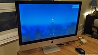 Front view of the Apple iMac showing the 27-inch display powered on at the login screen.