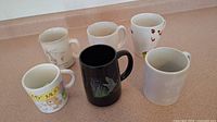Photo showing all six ceramic mugs on a countertop with varied designs and colors.