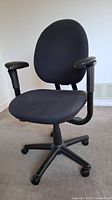 Front angle view of the black ergonomic office chair showing padded seat and backrest, adjustable armrests, and caster wheel base.