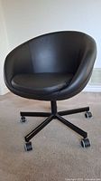 Front view of black faux leather swivel chair showing padded seat and curved backrest.