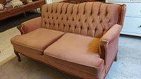 Front view of the sofa showing pink velvet upholstery, tufted back, and wooden armrest frames.