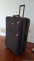 Side-front view of large dark grey nylon suitcase showing front pockets, telescopic handle extended, and two wheels.