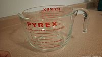 Clear glass Pyrex measuring cup with red measurement markings and ergonomic handle shown from front angle.