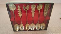 Set of 6 silver plated souvenir spoons with Hong Kong themed tops displayed inside original case with red lining and clear lid.