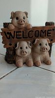 Front view of plastic pig welcome sign featuring three pig figurines and 'WELCOME' lettering on rustic wood-style plank.