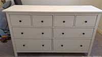 Front view of white Ikea 8-drawer dresser made of wood with black hardware knobs, showing minor stains on top.