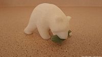 Photo of the white stone polar bear figurine holding a green jade fish showing overall side profile on cork surface.
