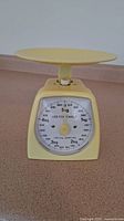 Front view of yellow mechanical kitchen scale showing dial and platform