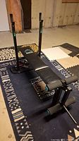 View of the entire workout bench positioned on patterned mat, showing the padded seat, metal frame, and adjustable stands.