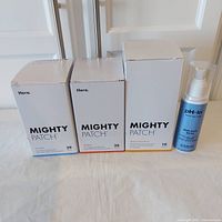 Photo with all 3 types of Mighty Patch boxes and pH-In body acne spray bottle lined up side by side on a flat surface.