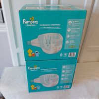 Two sealed teal Pampers Baby Dry diaper cases stacked, showing front and side packaging with brand and product details.