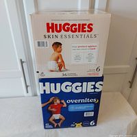 Photo showing two stacked sealed cases of Huggies diapers. The top box is Huggies Skin Essentials, and the bottom box is Huggies Overnites.