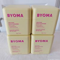 Four Byoma Melting Balm Cleanser containers stacked in two rows, showing front labels with product name and key ingredients.
