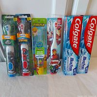 Full lot showing four branded kids' powered toothbrushes and two Colgate toothpaste tubes in original sealed packaging.