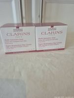 Two boxed jars of Clarins Super Restorative Day Cream placed side by side on a light surface.