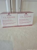 Two boxed jars of Clarins Super Restorative Day Cream side by side showing front faces with branding and product description.