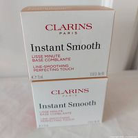 Two boxed Clarins Instant Smooth skincare products stacked, showing front text with product name and size.