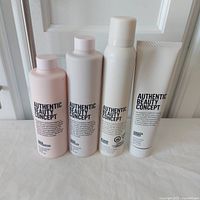 Four bottles/tubes of hair care products from Authentic Beauty Concept arranged side by side on a white surface. From left to right: Glow Conditioner, Glow Cleanser, Amplify Mousse and Shaping Cream.