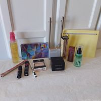 Full lot of cosmetics arranged on table showing various products including Bioderma cleaning oil, makeup palettes, primers, lipsticks, powders, setting spray and cosmetic bag.