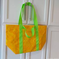 Front view of large yellow floral print tote bag with green handles hanging on cabinet handles.