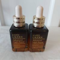 Two amber glass bottles of Estee Lauder Advanced Night Repair with gold and white dropper caps.