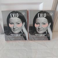 Two sealed boxes of Evio Pink Perspective Hydrogel Eye Therapy Patches shown upright with front label showing a woman's face with pink patches under eyes.