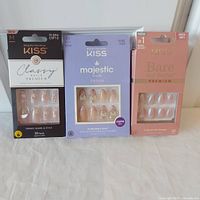 Three unopened boxes of Kiss false nails: Classy Premium, Majestic Dream, and Bare but Better Premium, displayed side by side on white surface.