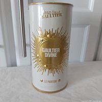 Front view of Jean Paul Gaultier Divine Le Parfum white and gold cylindrical can with decorative gold emblem and branding.