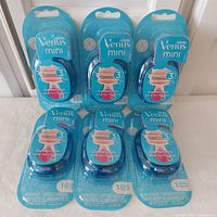 Six Gillette Venus Mini Comfortglide White Tea razors in sealed packaging arranged in two rows of three.
